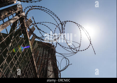 old metal steel gate in run down buildings protected with corrugated metal and sharp razor wire fence as keep out Stock Photo