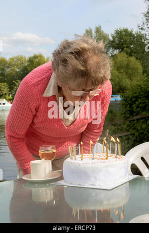 A mature retired elderly woman blowing out candles on her birthday cake, UK Stock Photo