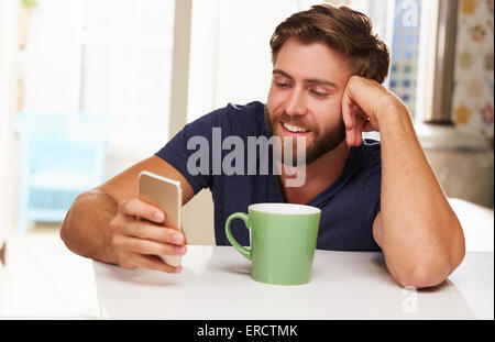 Young Man Drinking Coffee And Using Mobile Phone At Home Stock Photo