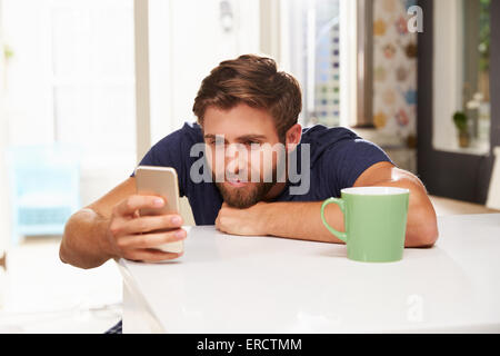 Young Man Drinking Coffee And Using Mobile Phone At Home Stock Photo