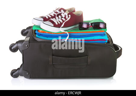 Ordinary wheeled black suitcase packed with bright summer clothes, sneakers, and sunglasses. Isolated on white Stock Photo