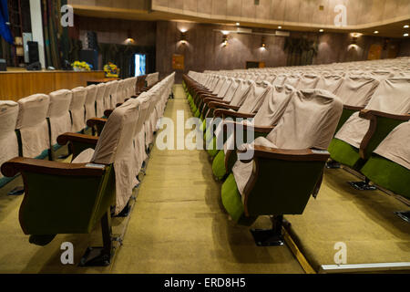 Side View of Rows of Empty Seats with Seat Covers in Well Lit Empty Theater Stock Photo