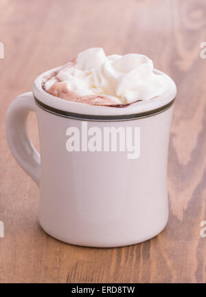 Hot chocolate with cream topping in an antique cup on rustic wooden table Stock Photo