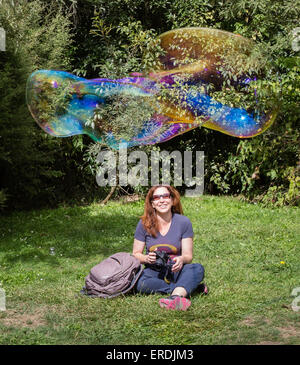 A happy smiling woman with a camera watches a newly formed giant soap bubble float past her Stock Photo