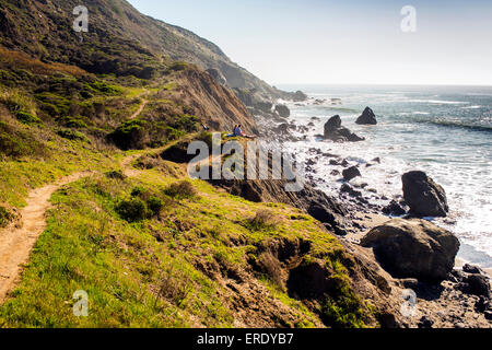 People sitting on rocky coastline trail near ocean Stock Photo