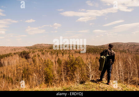 Caucasian man with camping gear overlooking rural forest Stock Photo