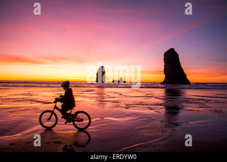 Silhouette of Caucasian girl biking near rock formations on Cannon Beach, Oregon, United States
