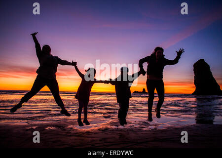 Silhouette of Caucasian family jumping for joy on Cannon Beach, Oregon, United States