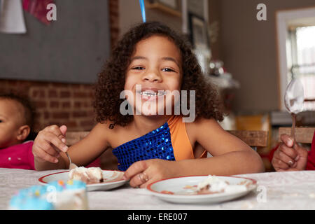 Mixed race girl eating cake at table Stock Photo