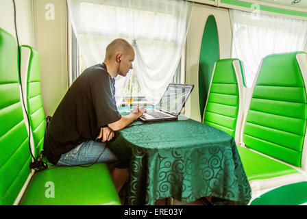 Caucasian man using laptop in green booth on train Stock Photo