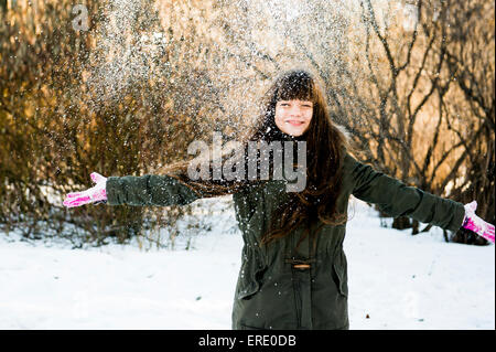 Caucasian girl throwing snow in field Stock Photo