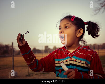 Mixed race girl blowing bubbles in field Stock Photo