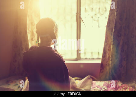 Mixed race girl looking out bedroom window Stock Photo