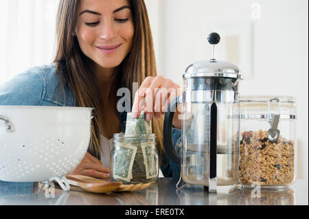 Caucasian woman putting money in jar Stock Photo