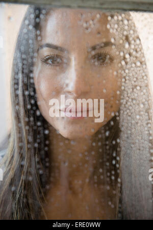 Caucasian woman peering through wet window Stock Photo