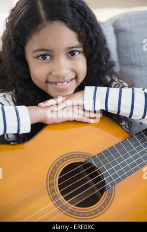 Mixed race girl holding guitar on sofa Stock Photo