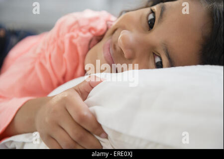 Close up of mixed race girl smiling on pillow Stock Photo