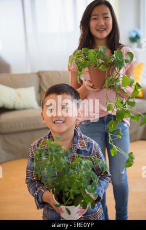 Asian brother and sister holding potted plants in living room Stock Photo