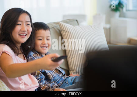 Asian brother and sister watching television on sofa Stock Photo