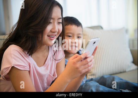Asian brother and sister using cell phone on sofa Stock Photo