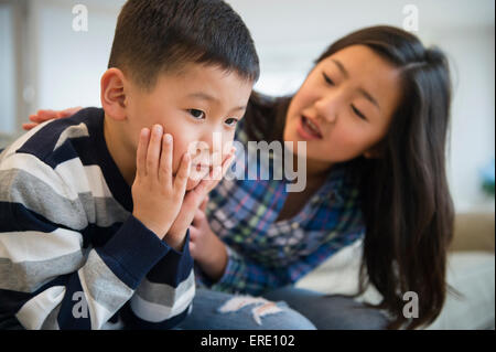 Asian sister comforting sad brother on sofa Stock Photo