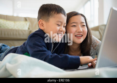 Asian brother and sister using laptop on living room floor Stock Photo