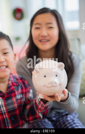 Asian brother and sister holding piggy bank in living room Stock Photo