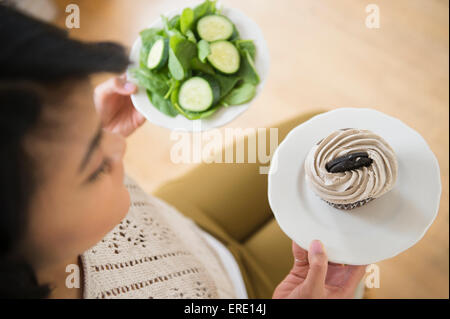 Pacific Islander woman choosing between cupcake and salad Stock Photo