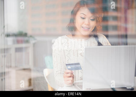 Pacific Islander woman shopping online on laptop behind window Stock Photo