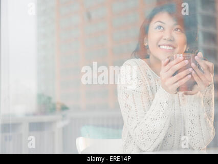Pacific Islander woman drinking cup of coffee behind window