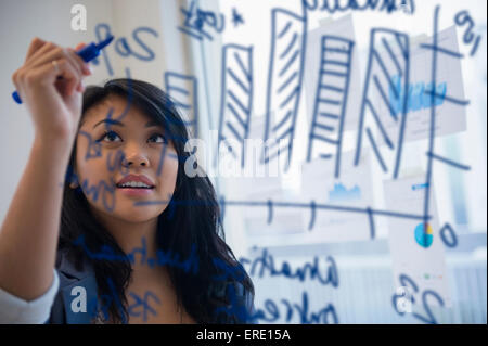 Pacific Islander businesswoman drawing chart on glass in office Stock Photo