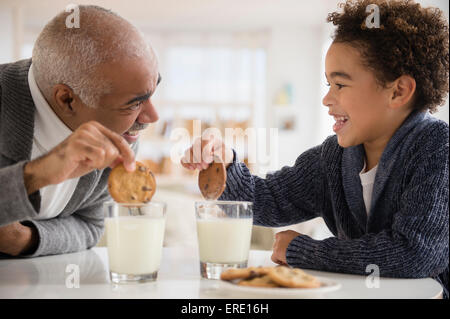 Mixed race grandfather and grandson eating cookies and milk Stock Photo