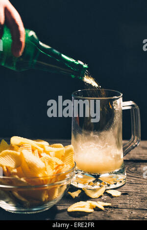 Hand pouring glass of beer near potato chips Stock Photo
