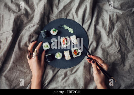 Hands of woman reaching for platter of sushi on bed Stock Photo