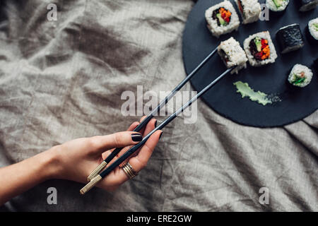 Hand of woman reaching for platter of sushi on bed Stock Photo