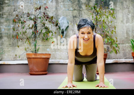 Older Caucasian woman practicing yoga in courtyard Stock Photo