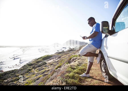 Black man texting cell phone near car at coast Stock Photo