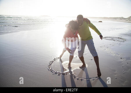 Couple drawing heart in sand on beach Stock Photo