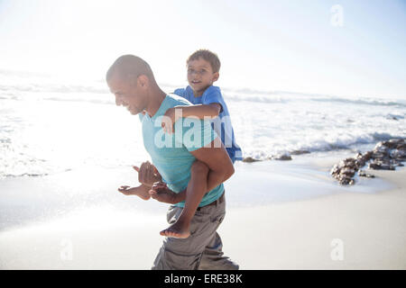 Mixed race father carrying son piggyback on beach