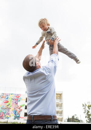 Hispanic father throwing son in air outdoors Stock Photo