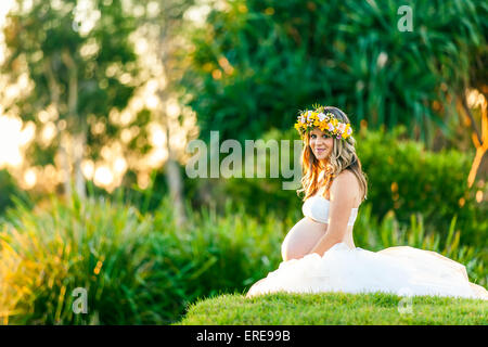 Young smiling pregnant woman in white dress with flowers in her hair Stock Photo