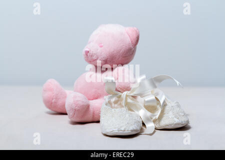 White lace baby booties and a cute pink teddy bear. Stock Photo