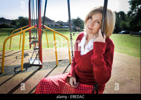 A woman in red sat on a swing in a park. Stock Photo