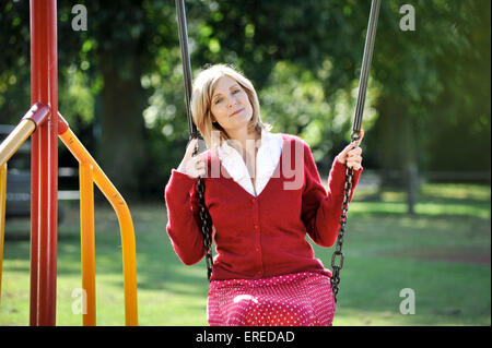 A woman in red sat on a swing in a park. Stock Photo