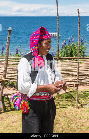 Smiling Taquileño man with traditional bright knitted cap and local dress, knitting, Taquile Island, Lake Titicaca, Peru Stock Photo