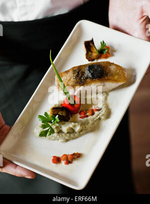 Roasted sea bass filet with soft olive tapenade, aubergine caviar and baby artichoke barigoule. Stock Photo