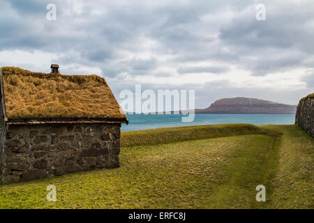 Traditional hut in the Faroe Islands with a green grass roof with a backdrop of the Atlantic ocean and an island Stock Photo