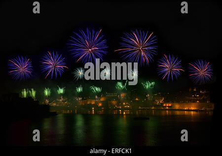 Fireworks. Fireworks explosion in dark sky with city sillouthe and colorful reflect on water in Valletta, Malta. Violet firework Stock Photo