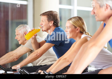 Thirsty man drinking orange juice in gym on spinning bike Stock Photo