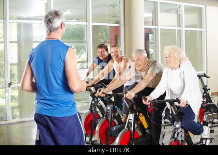 Senior people in rehab care center with instructor riding spinning bikes in gym Stock Photo
